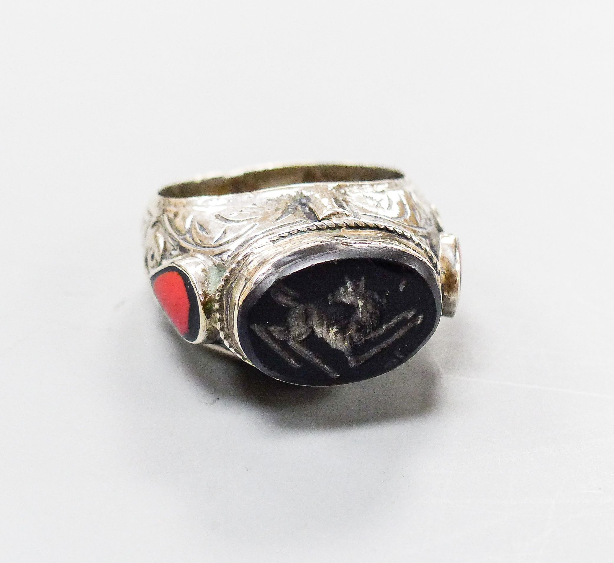 A continental engraved white metal and oval intaglio black onyx ring, with two colour enamel set shoulders, size S/T, gross weight 18.8 grams.